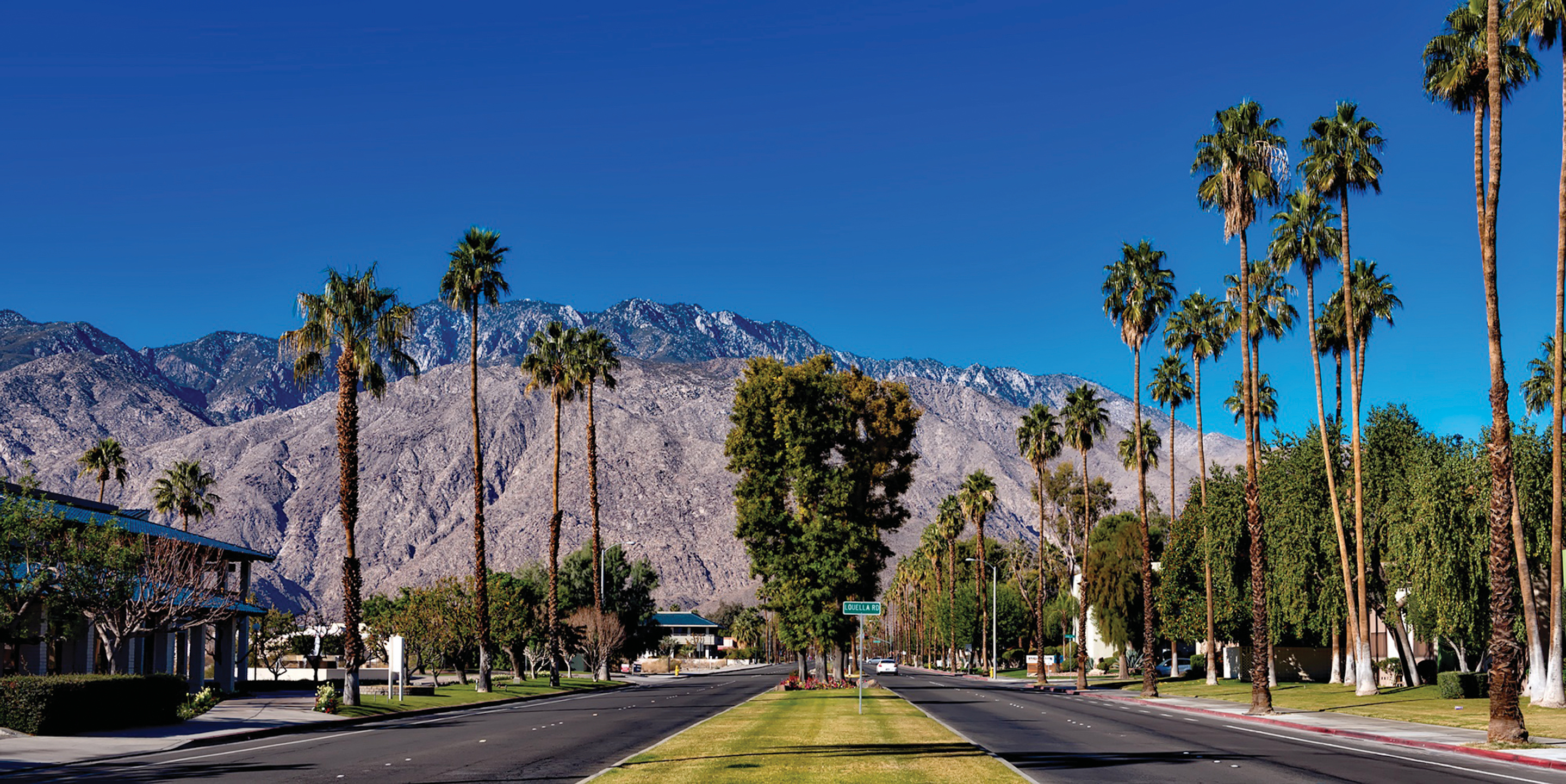 A two-way road showing palm trees and mountains