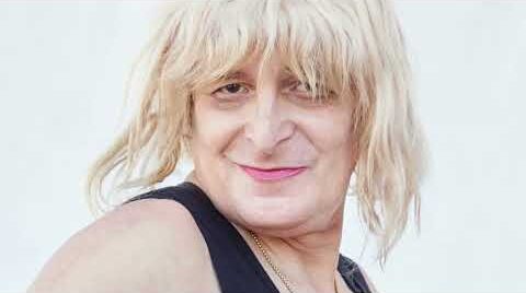 Person with blonde hair in a black tank top smiling at the camera against a white background.