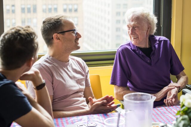 Group of three people sitting together and talking near a window with city buildings in the background