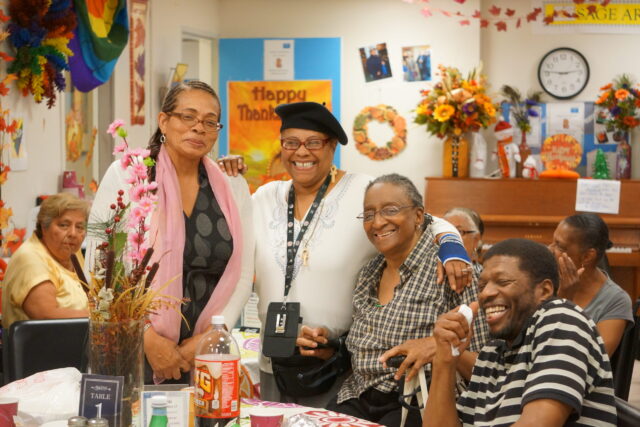 People smiling and posing together in a colorful community room with festive decorations on the walls.